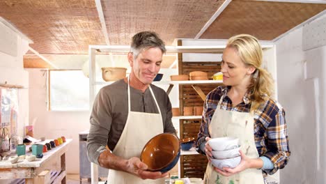 Male-and-female-potters-holding-pottery-in-workshop