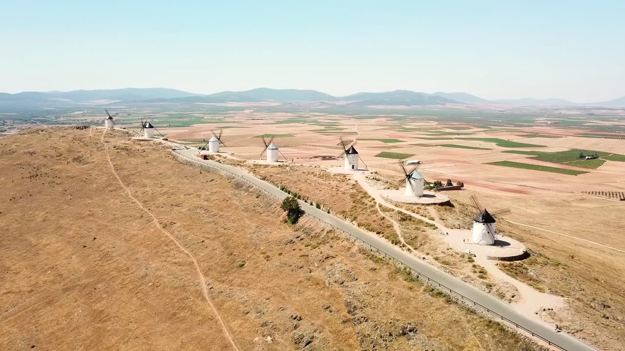 Aerial view capturing the historic windmills - molinos de viento- of Consuegra atop a hill, overlooking the arid plains of Castilla–La Mancha, embodying the region's cultural heritage, drone shot