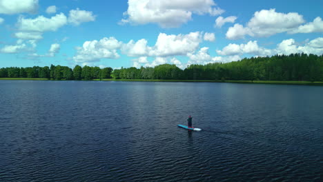 drone pullback: lone paddleboarder on tranquil lake amidst verdant trees