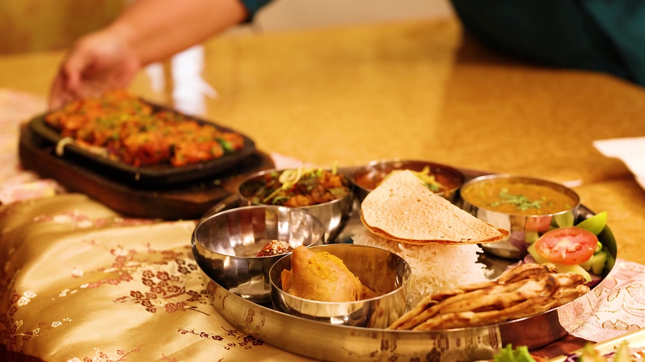 En tjener placerer en varm sydende tallerken ved siden af et varieret indisk thali-måltidsfad.
