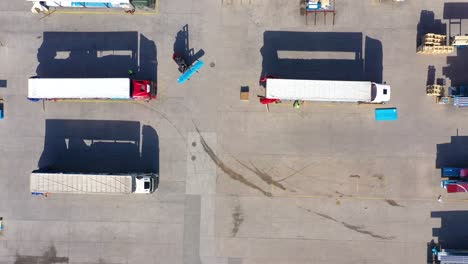 Semi-truck-with-cargo-trailer-is-travelling-on-a-parking-lot-along-a-warehouse-of-a-logistics-park