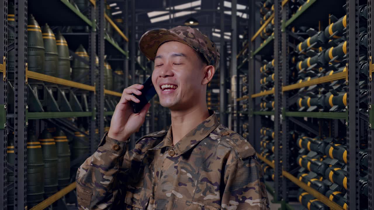 Primo piano laterale di un soldato asiatico che parla al telefono e si guarda intorno mentre si trova in un deposito di munizioni militare