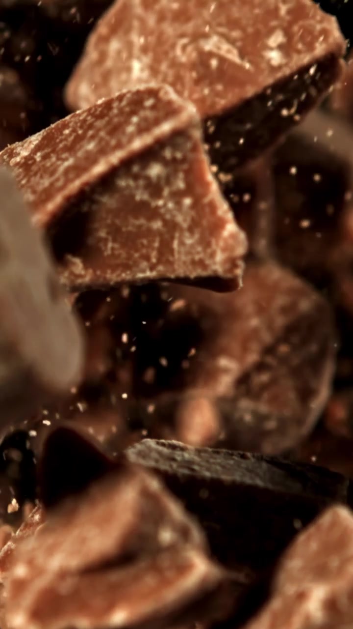 Deliziosi pezzi di cioccolato e polvere di cacao che cadono al rallentatore