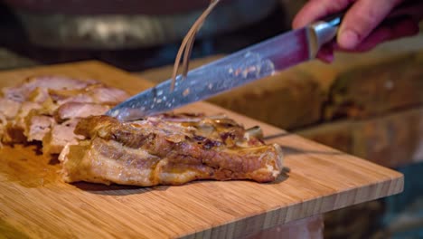 primer plano de un chef cortando tiernas rebanadas de carne de cerdo cerca de un horno de leña
