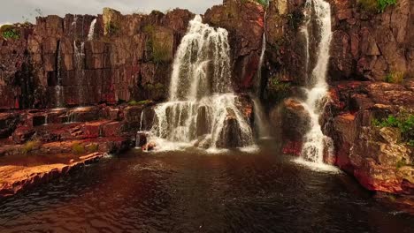 Slow-motion-aerial-shot-flying-towards-a-small-waterfall-on-a-rocky-cliff-face