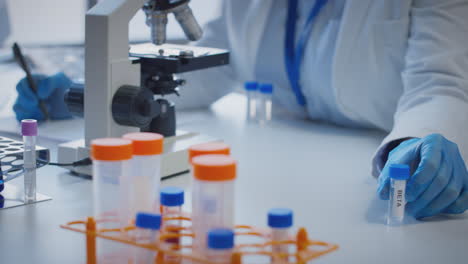 Close-Up-Of-Lab-Worker-Conducting-Research-Using-Microscope-Holding-Test-Tube-Labelled-Beta