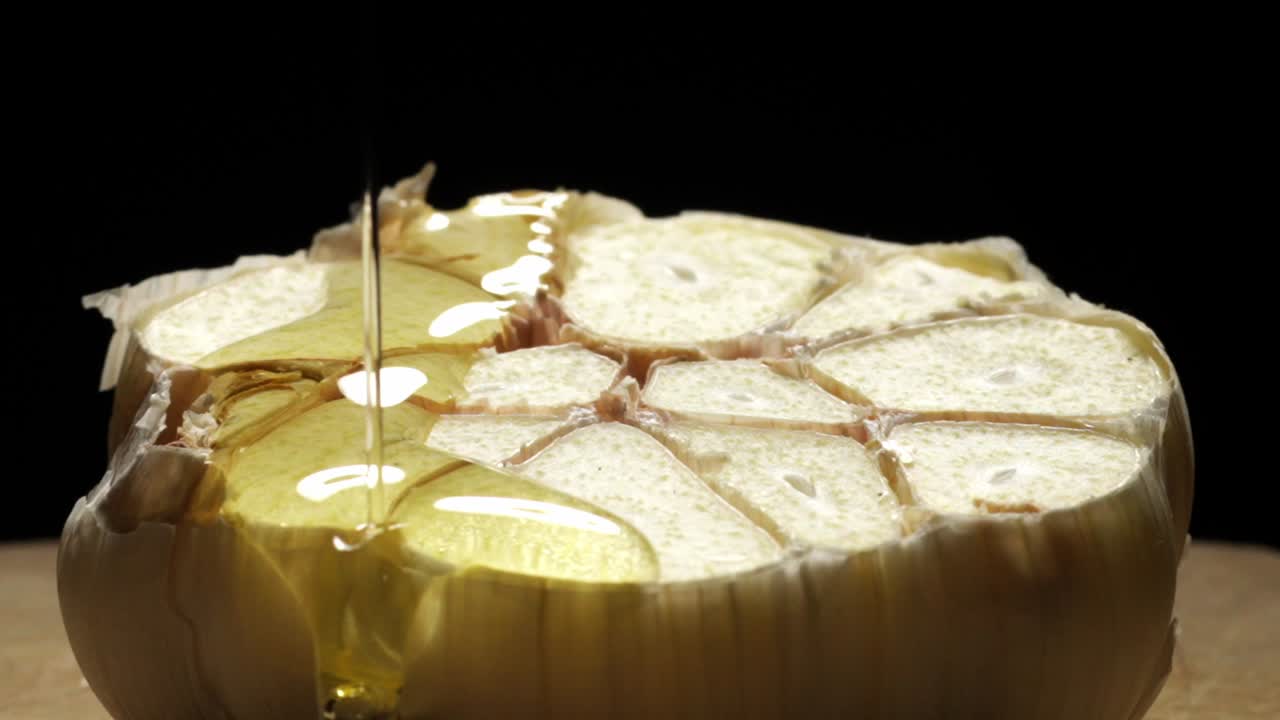 Macro Shot, Pouring Oil On Half Sliced Garlic Bulb Against Black Background, Slow Motion