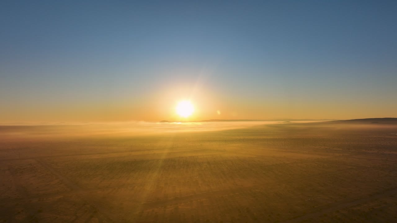 Golden sunrise over misty landscape, light rays piercing through haze, serene morning vibe