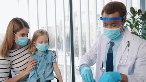 Porträt-Eines-Jungen,-Gutaussehenden,-Glücklichen-Mannes,-Arztspezialist,-Immunologe-In-Maske,-Der-Süßes-Kleines-Mädchen-Injiziert,-Das-Mit-Mutter-In-Der-Klinik-Sitzt,-Krankheitsprävention,-Impfkonzept