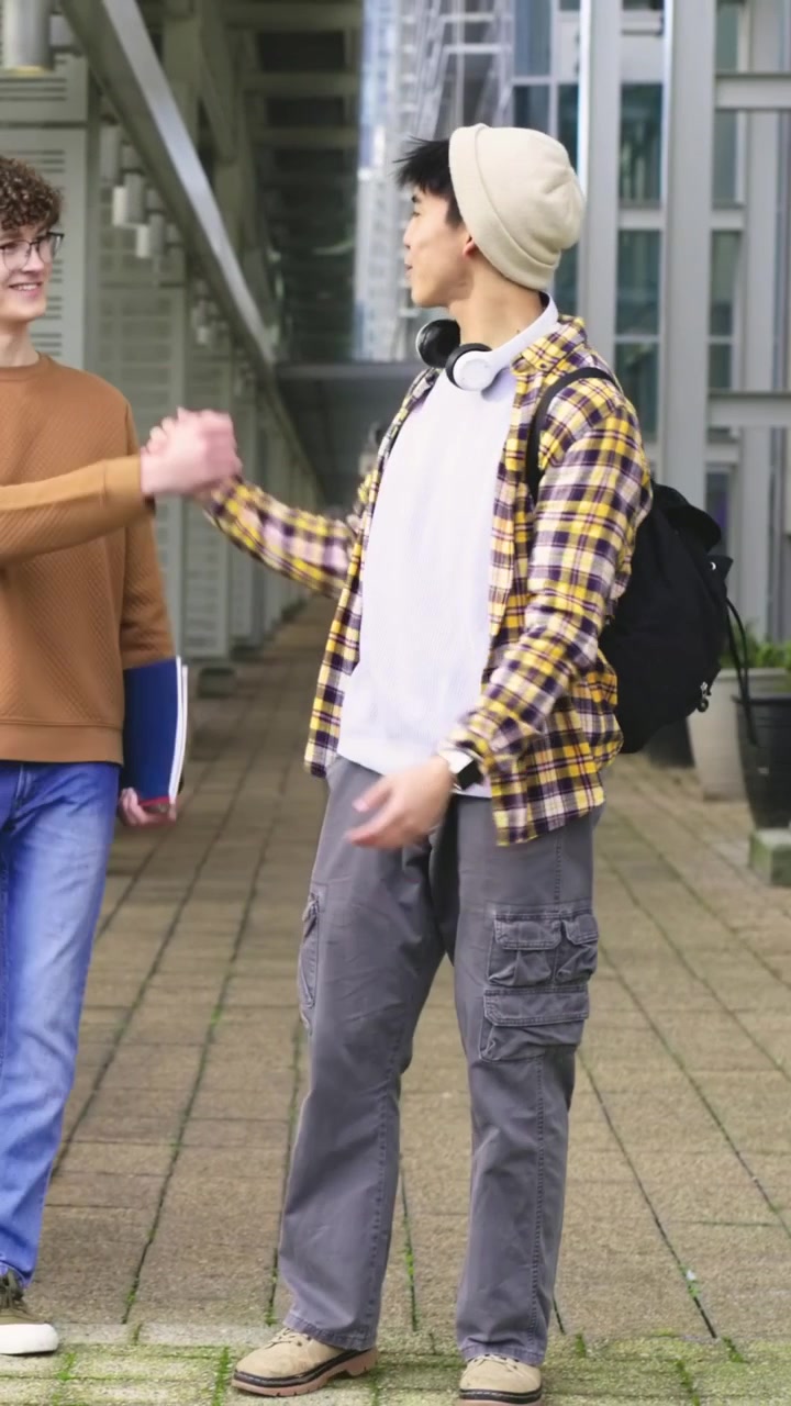 Video verticale: Studente con berretto che cammina scorrendo il telefono su un marciapiede mentre il telefono vibra, incontrando un amico.