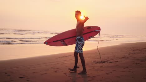 hunky surfer carries board to water sunrise shaka brah signal