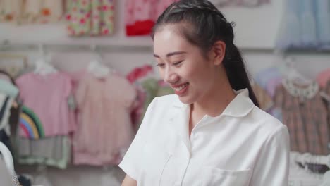 close up of asian mother choosing one of kids clothing items on hangers then smiling and showing a credit card to the camera while shopping at the boutique