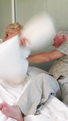 una pareja de mayores haciendo una pelea de almohadas.