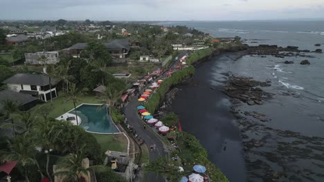 low aerial flies over black volcanic sand beach cliffs at cemagi, bali