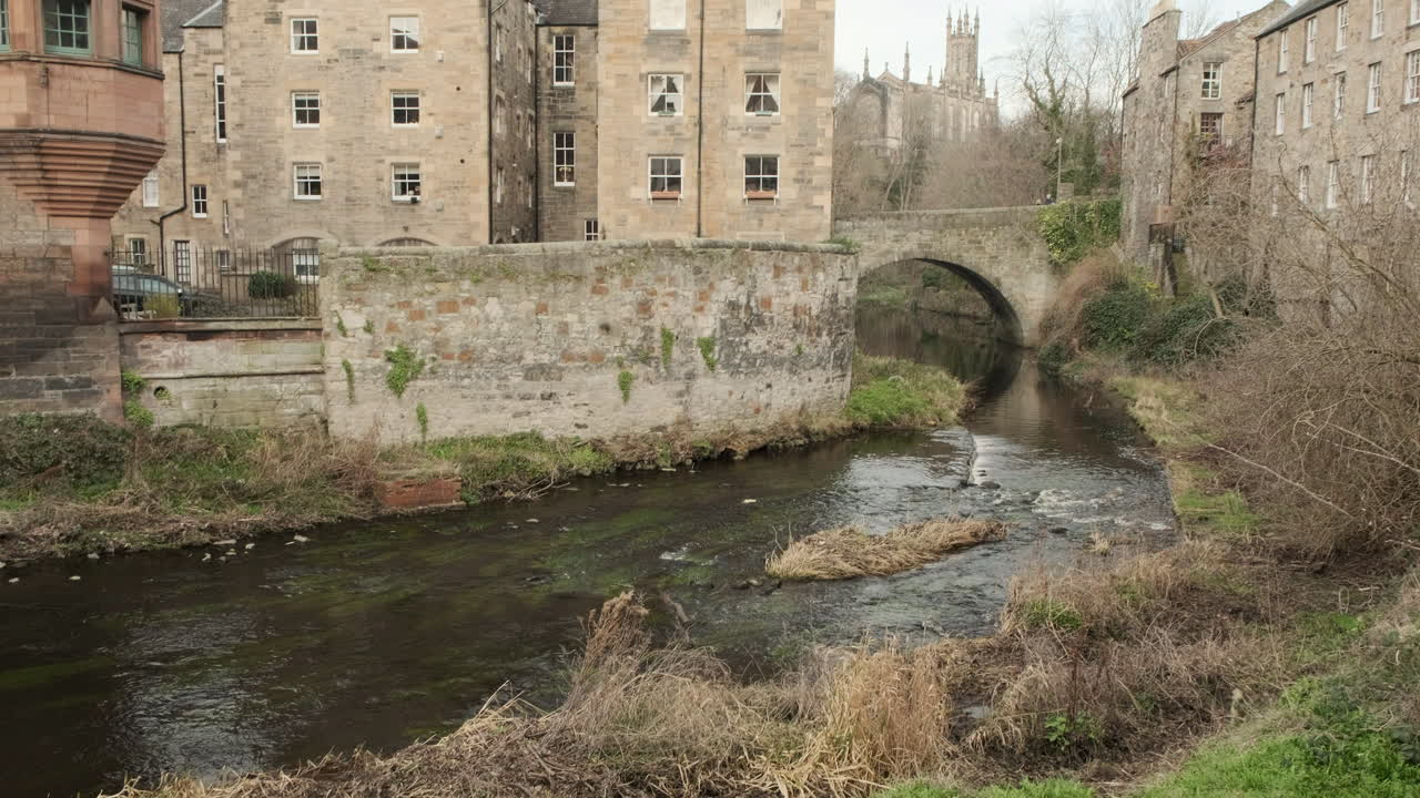 Diagonal pan from lower left to upper right from the Water of Leith river next to Dean Village Well Court over to Rhema Christian Centre Church on an overcast day in Edinburgh, Scotland