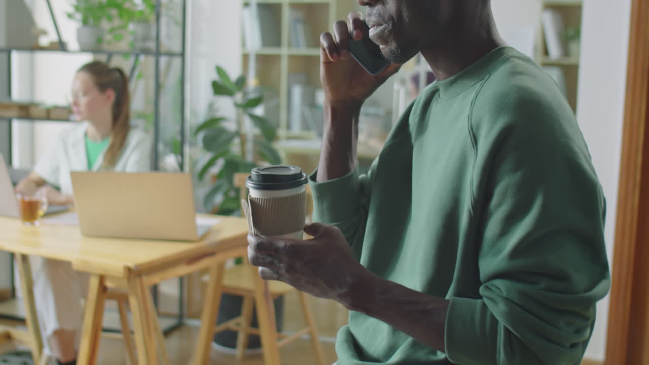 Black Man With Coffee Cup Calling on Phone in Office