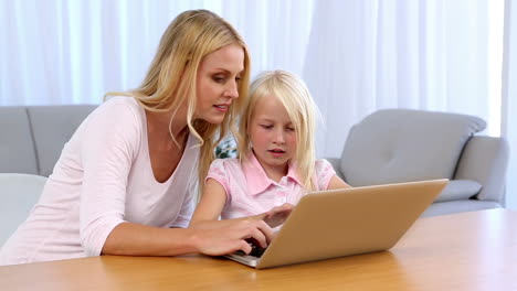 mother and daughter sitting at table and using laptop