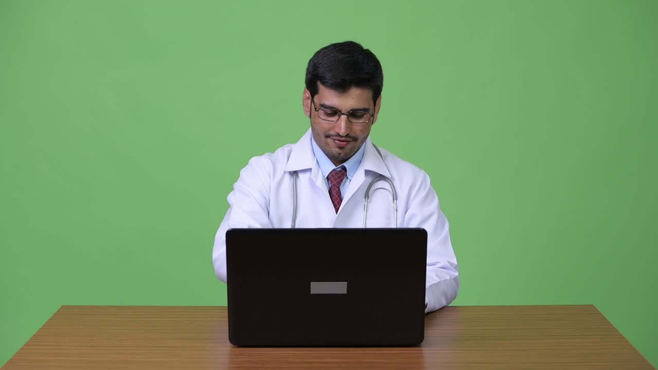 Young handsome Persian man doctor using laptop