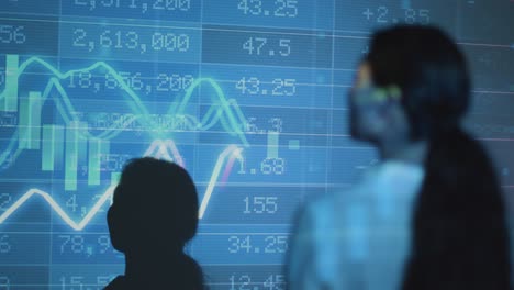 woman visiting immersive art exhibition with projection of shapes and patterns on wall with financial data