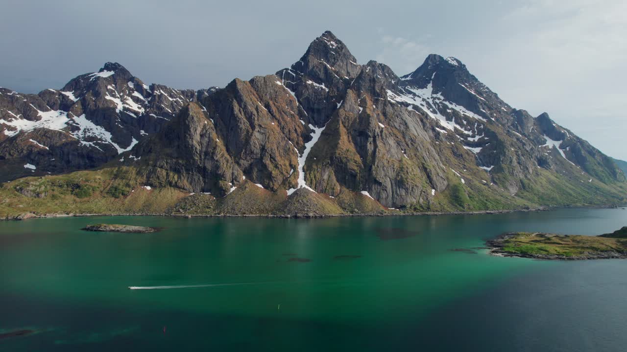 Breathtaking aerial view of a boat sailing on the turquoise waters of the Steinsfjorden, with the snow capped peaks of the Lofoten Islands in the background