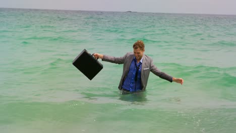 Front-view-of-Caucasian-Businessman-dancing-with-briefcase-in-the-sea-at-beach-4k