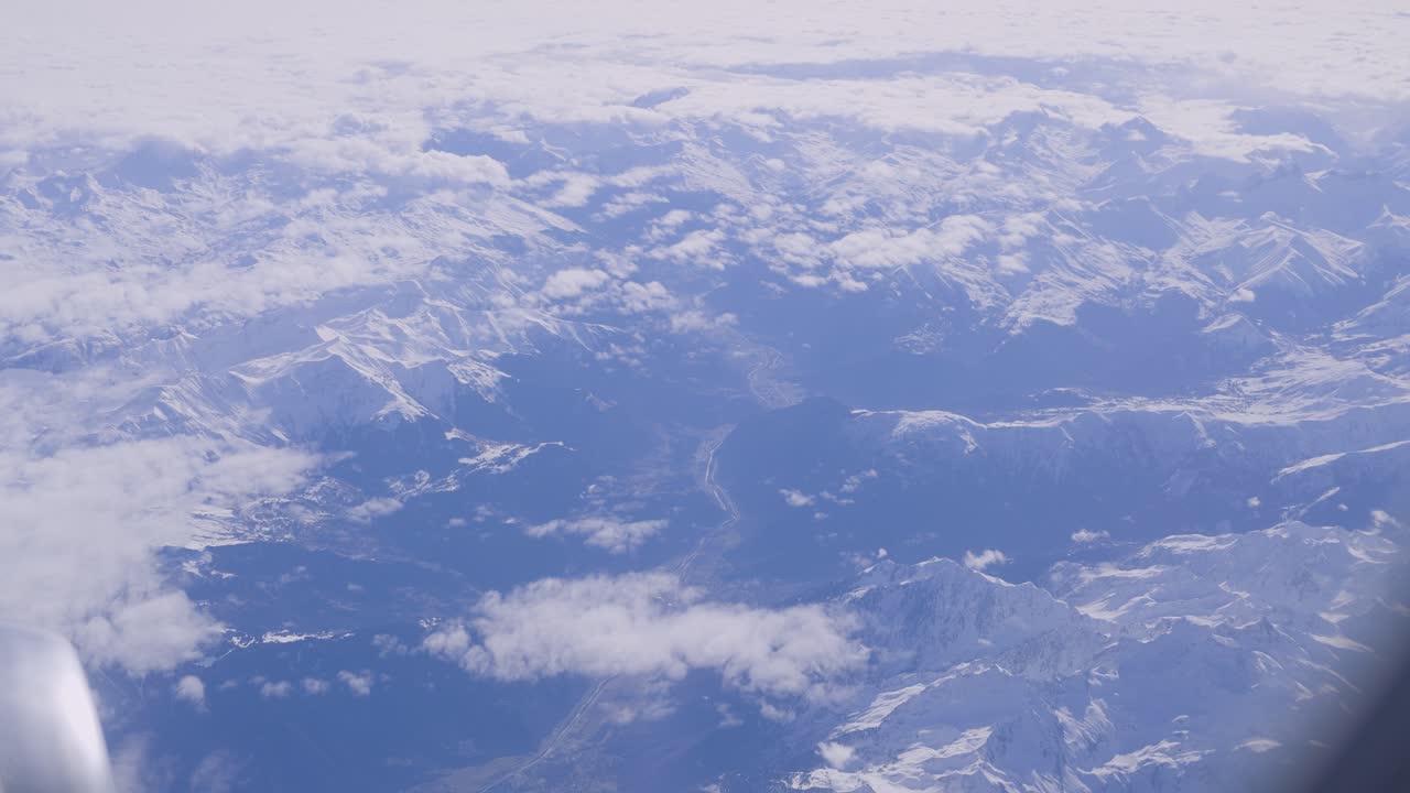 Snowy mountain range from passenger plane pov, clouds scattered above, aerial view