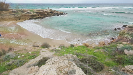 Aerial-view-of-a-secluded-beach-cove-with-turquoise-waters-gently-lapping-sandy-shores,-surrounded-by-rocky-outcrops-and-greenery