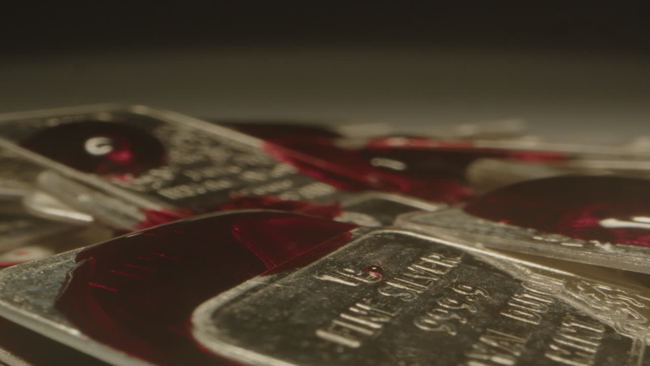 Macro view of blood slowly dripping on fine silver bars in slow motion. The blood slowly flows over the letters on the shiny plates