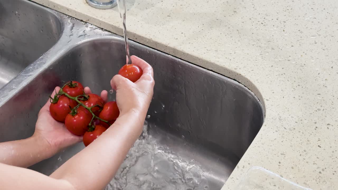 Hands rinse fresh vine tomatoes under running water in a bright, clean kitchen setting