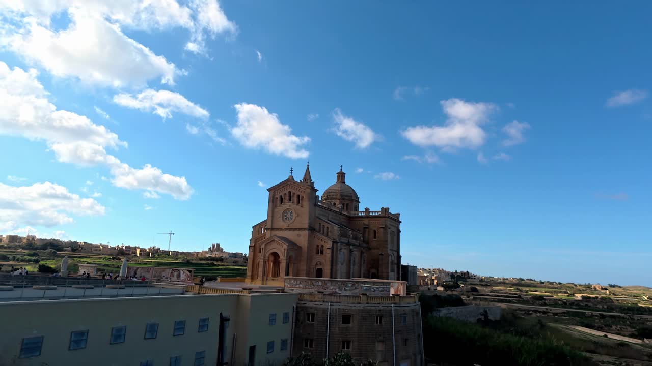 Il maestoso Santuario Nazionale di Ta' Pinu si erge sotto un cielo azzurro brillante durante una soleggiata primavera mediterranea a Gozo, Malta, mettendo in mostra architettura neoromantica e pietra calcarea dorata da un'ampia angolazione bassa
