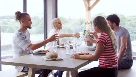 four young adult friends celebrate, pouring wine and raising glasses during a dinner party