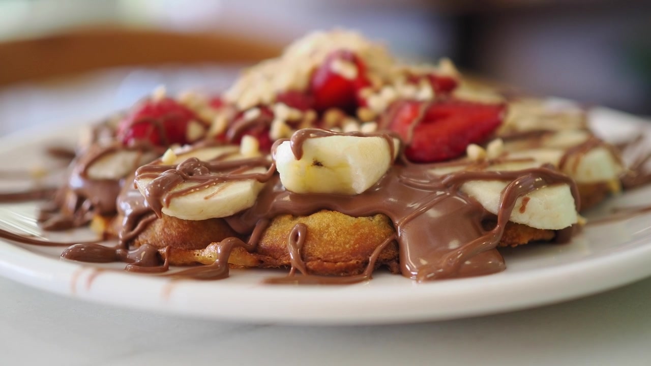 Delizioso waffle guarnito con cioccolato, fragole, banane e frutta secca