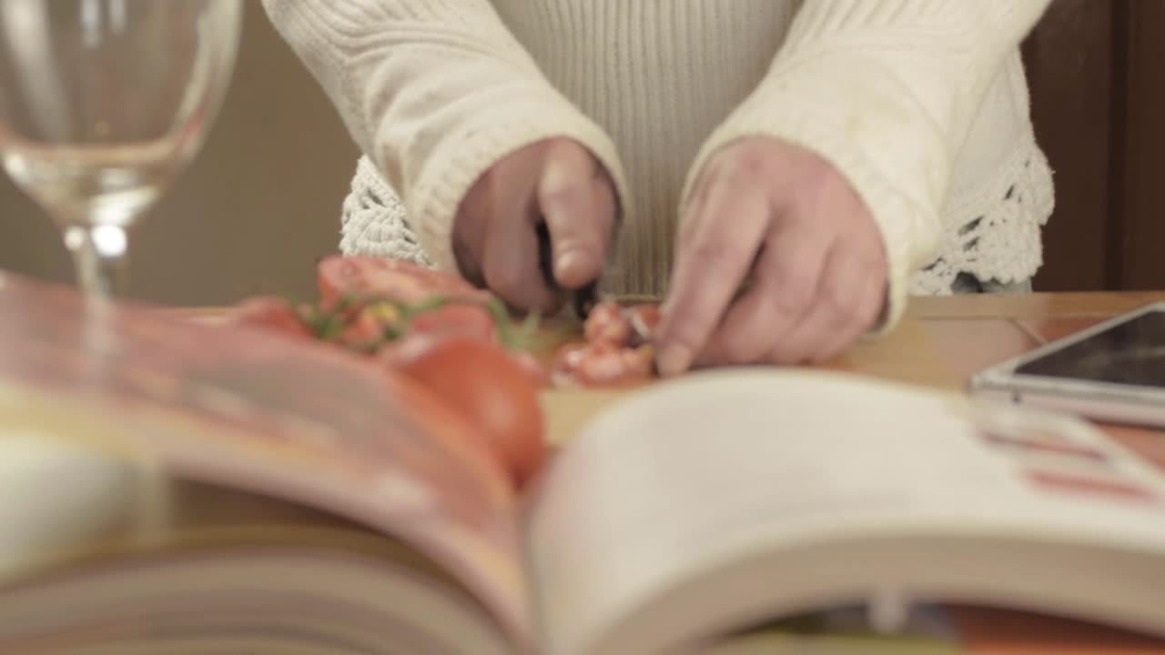 manos cortando tomates frescos en la cocina con el libro de recetas en primer plano.