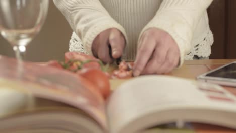 レシピ本を前景にしてキッチンで新鮮なつるトマトを切る手