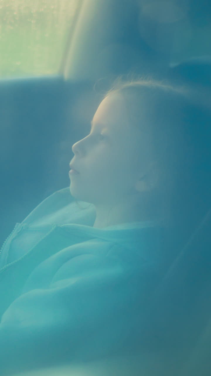 Pensive child waits for parents in car on rainy day. Depressed little girl sits along in auto under heavy rain storm. Abused kid in automobile at storm