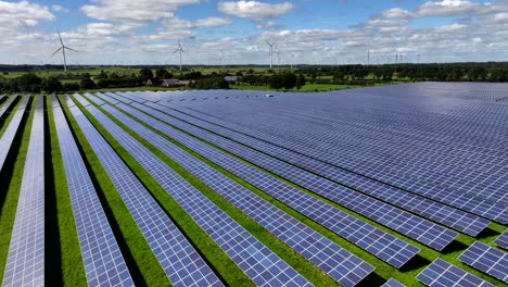 rows of photovoltaic solar panels in a solar farm generating clean and eco-friendly energy, aerial view, drone flight, wind turbines in the background