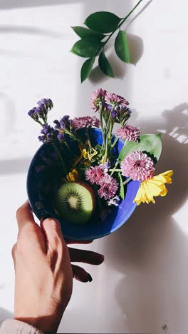 hand holding a bowl with flowers and kiwi