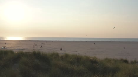 Filmische-Drone---Luftaufnahme-Des-Grünen-Und-Sandigen-Naturstrandes-Bei-Sonnenuntergang-Mit-Touristen-Und-Menschen-Beim-Buggykiten-In-Zeeland-An-Der-Nordsee,-Niederlande,-30p