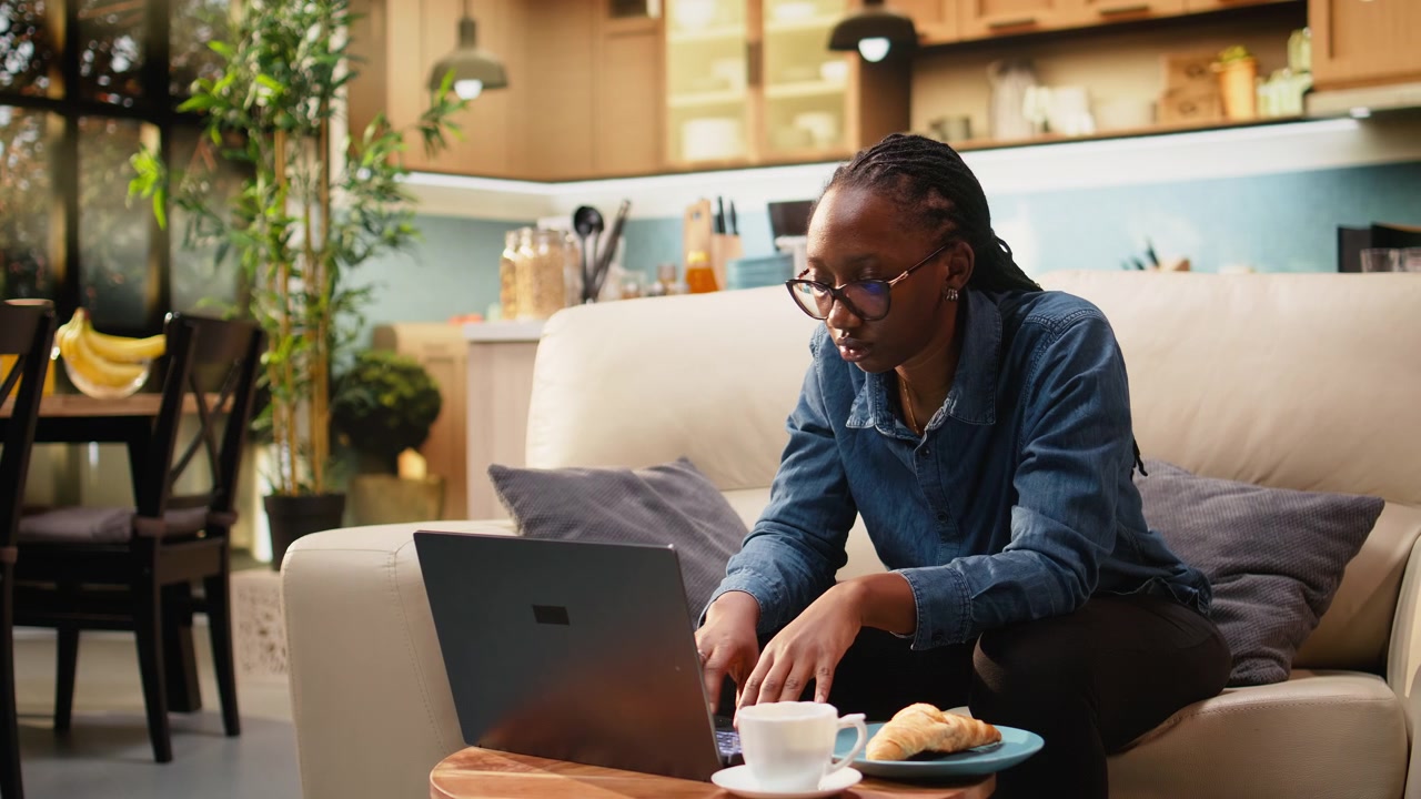 Young woman eating croissants and using laptop in home interior