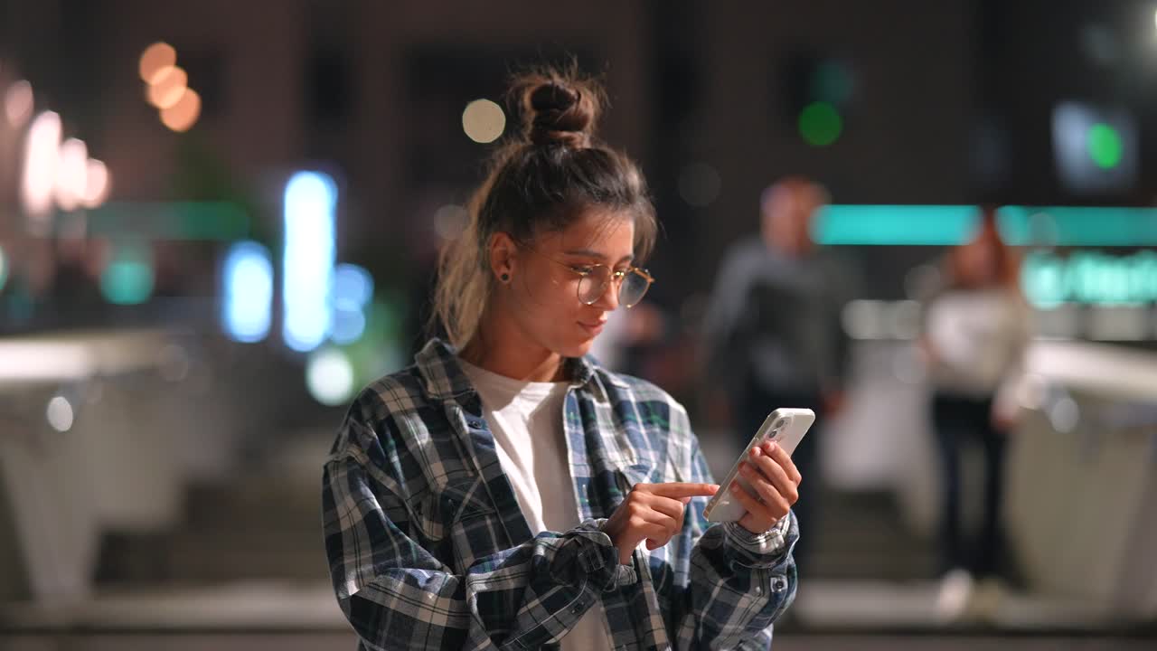 mujer joven usando un teléfono inteligente por la noche en la ciudad