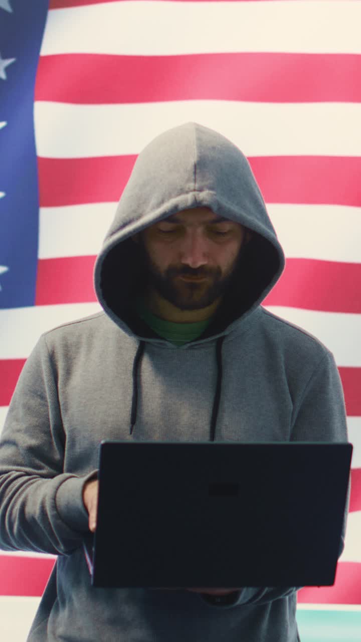 Uomo con felpa con cappuccio che usa un laptop di fronte alla bandiera americana