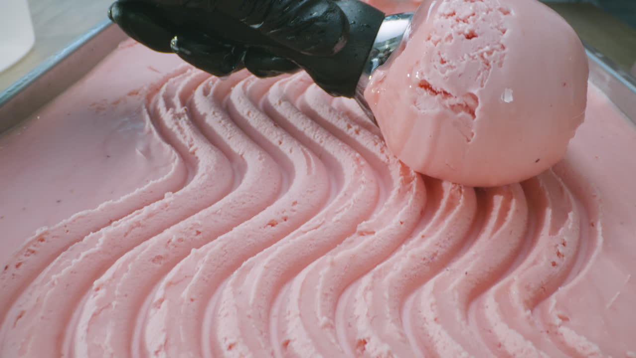 A close-up of pink lemonade ice cream, with a vibrant color and smooth texture, being scooped out with a metal scoop. Refreshing, summery, and visually appealing.