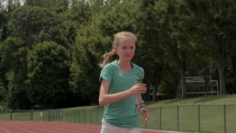 teen girl athlete runs track towards and past camera in slow motion