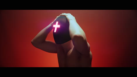 masked man with cross of light glowing on his face moves slowly