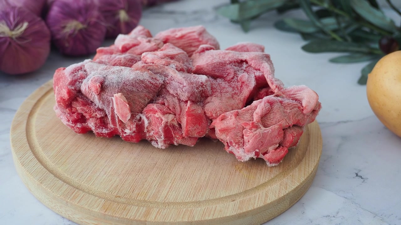 Frozen Raw Meat Chunks on Wooden Cutting Board