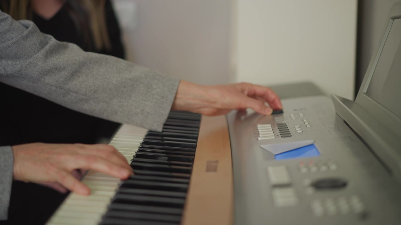 Mani dell'insegnante guidano lo studente sulla tastiera, l'istruttore regola le impostazioni mentre lo studente pratica accordi e dinamiche, luce soffusa in aula, atmosfera di coaching di supporto, stretta collaborazione e didattica