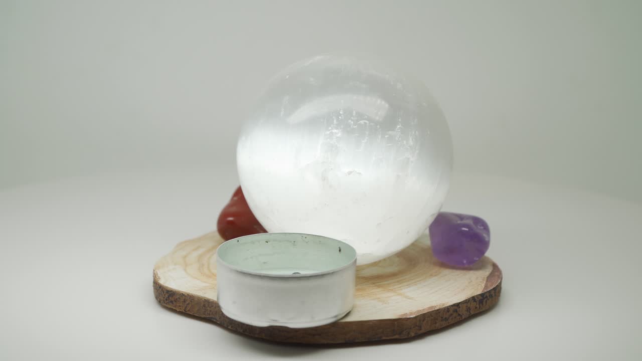 A Mirror Like Crystal Ball Sitting On A Piece Of Wood With Red Stone And Small Candle Holder - Close Up Shot