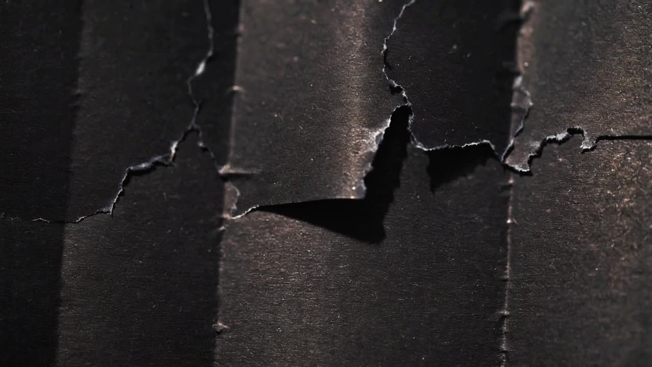 Grazing upper-left light causing torn dark paper flap shifting closeup showing void, ridged texture