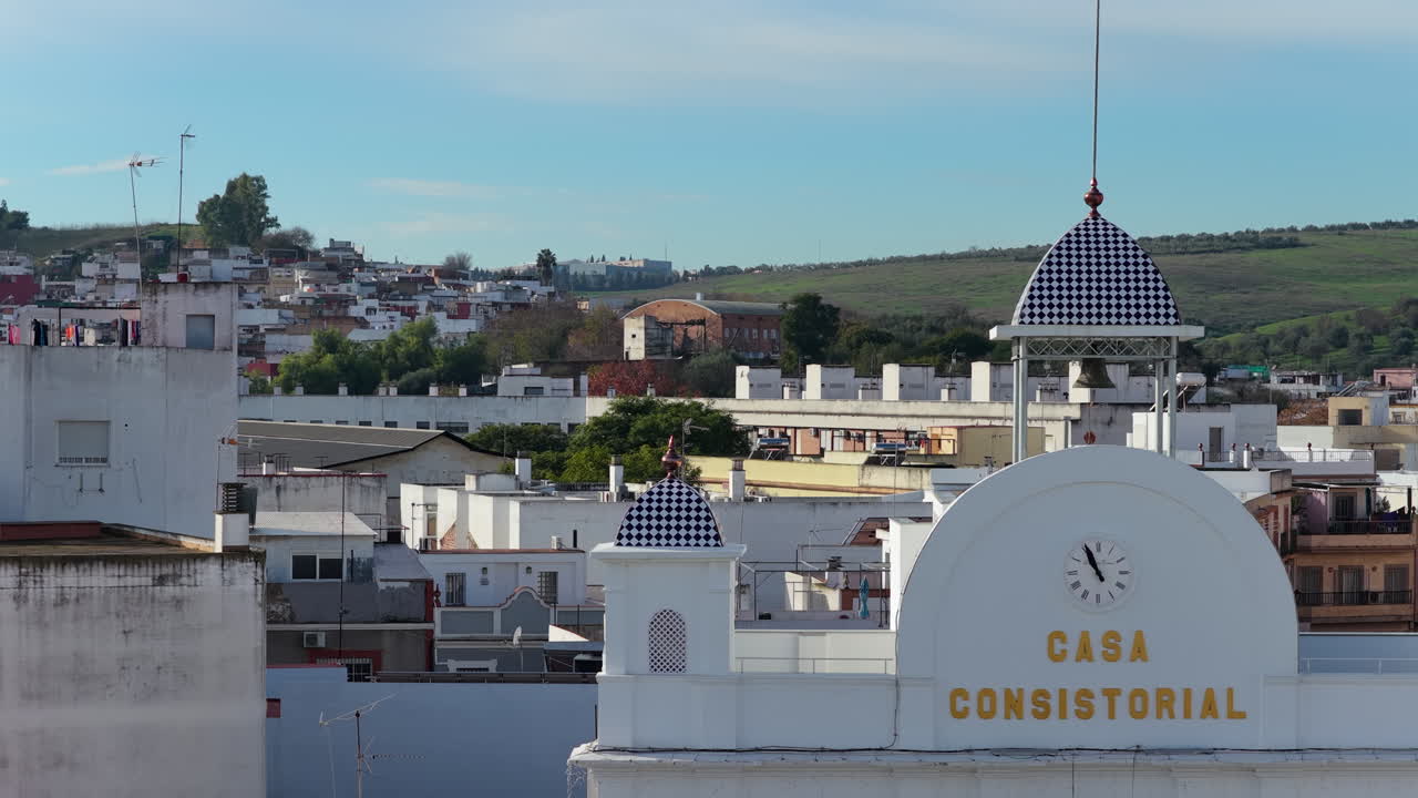 Slider aereo destro focalizzato sui dettagli architettonici del municipio di Camas (Casa Consistorial), con scritte dorate, quadrante dell'orologio e caratteristici piramidi del tetto a scacchi blu e bianchi