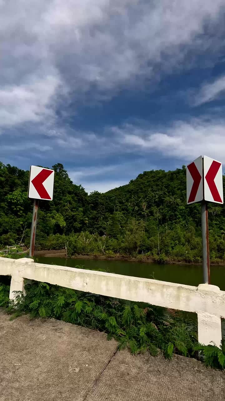 Punto di vista spontaneo dall'auto che mostra una strada di campagna rurale con un fiume e colline boscose che conducono a Sugar Beach a Sipalay, Negros Occidental, Filippine.